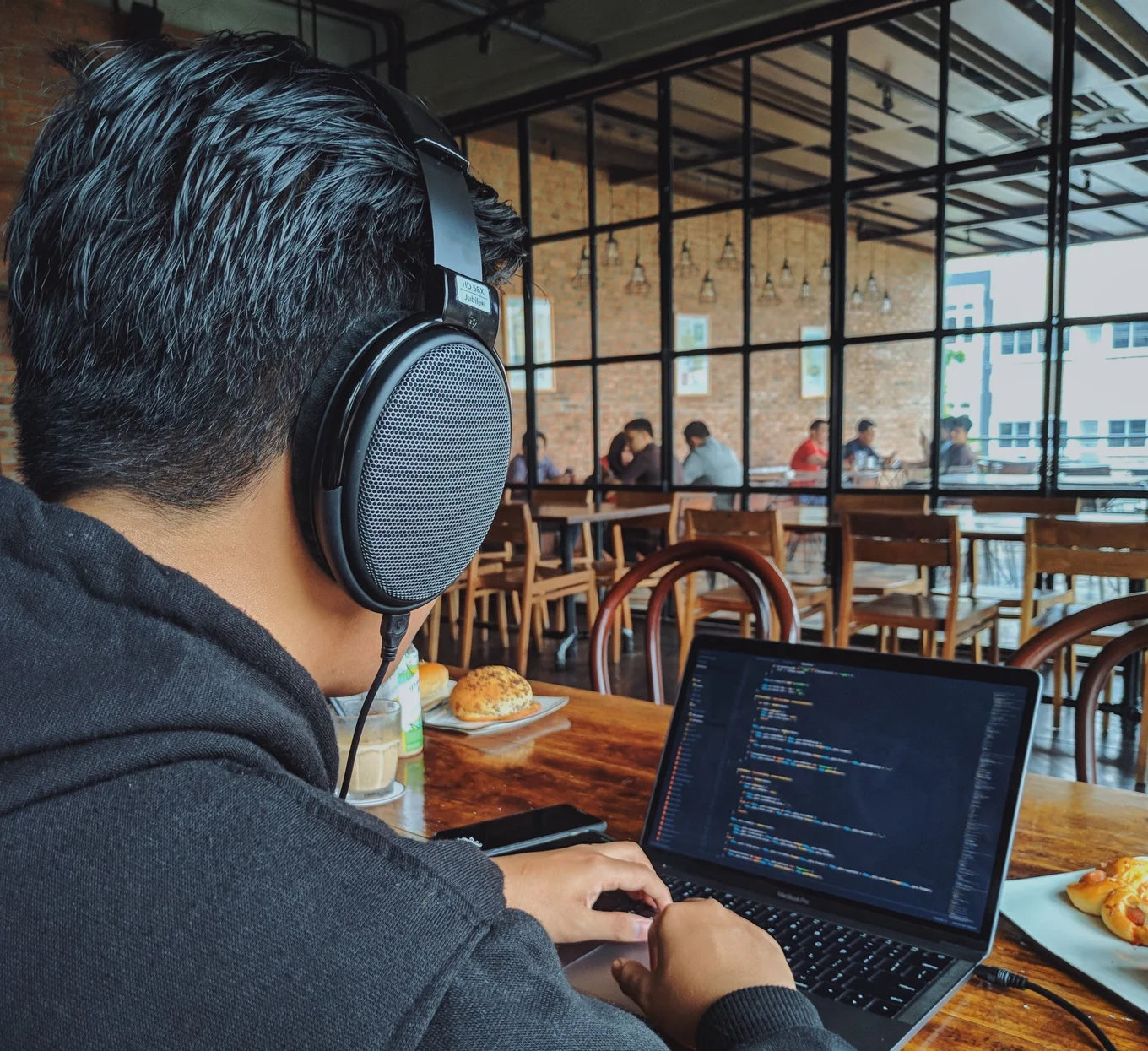 Person wearing headphones, using laptop in cafe.
